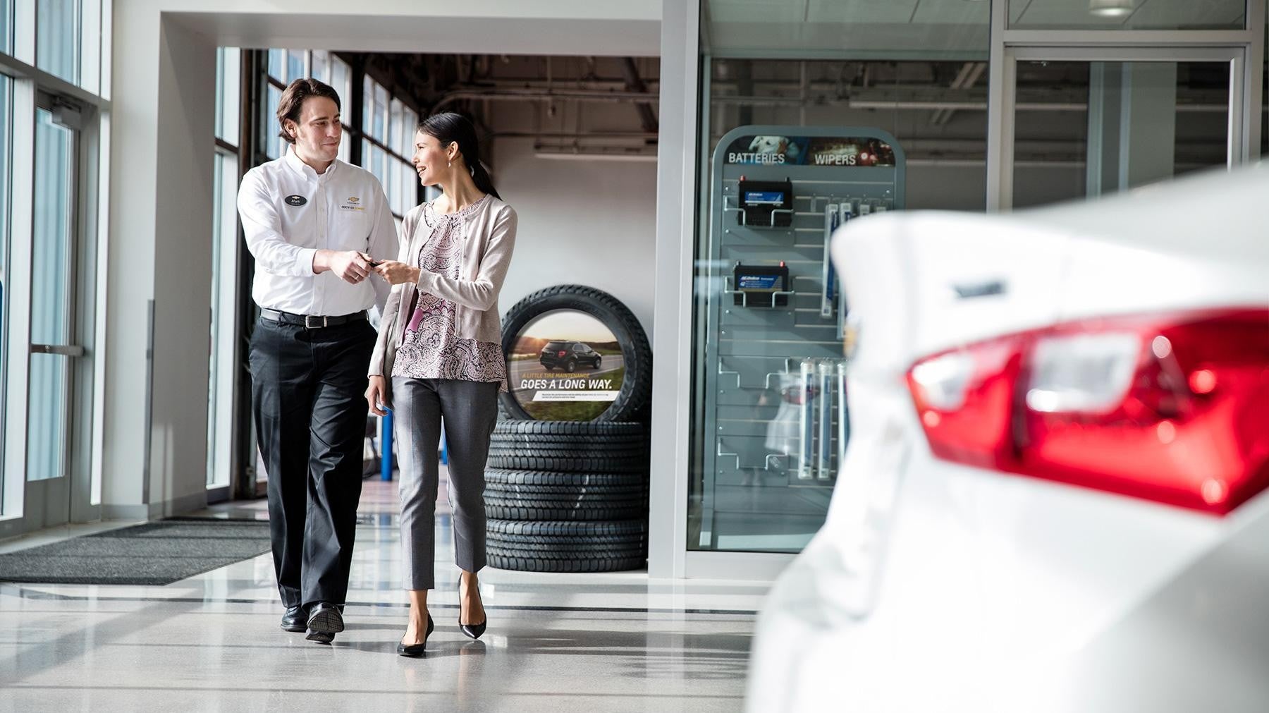Dealership employee and customer walking through a showroom with cars and tire displays.