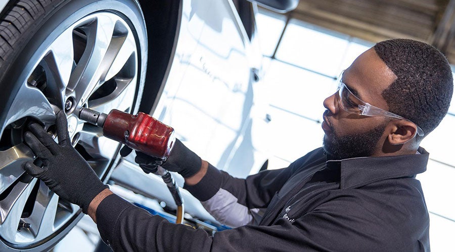 Mechanic tightening a tire lug nut using a red impact wrench on a car.