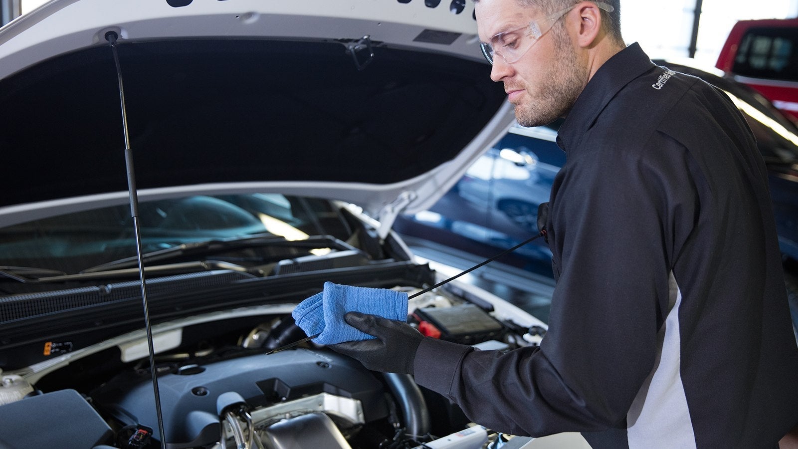 Technician checking the oil level with a dipstick and a blue cloth under an open car hood.