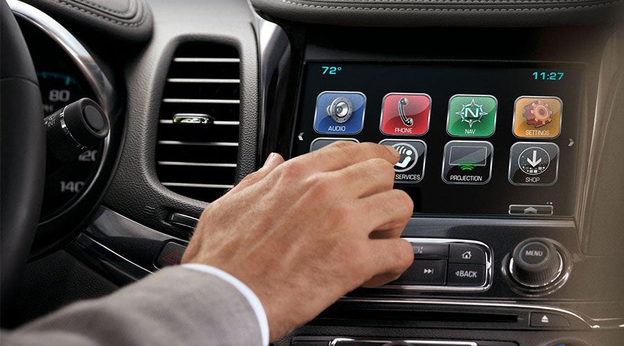 A hand touching a car's infotainment screen with various app icons