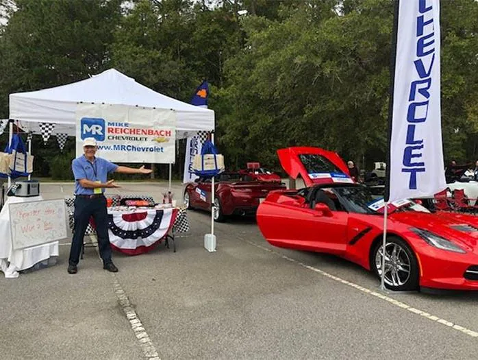 Man presents a Mike Reichenbach Chevrolet tent with red sports cars