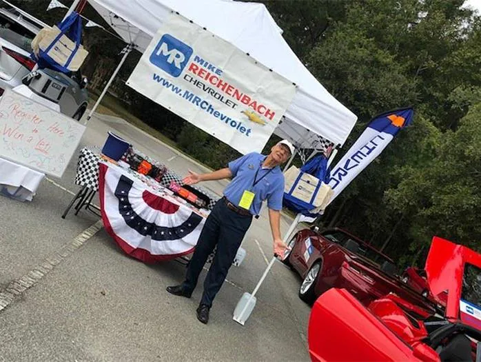 Man stands gesturing by the Mike Reichenbach Chevrolet event tent.
