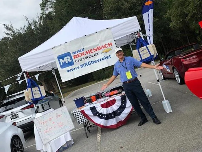 Man standing with open arms by a Chevrolet dealership display tent