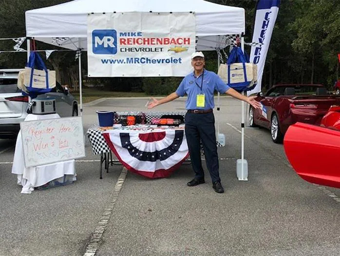 Man smiling with open arms at a Chevrolet dealership display.