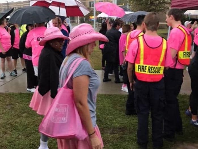 People, some wearing pink, gather for an outdoor event in the rain