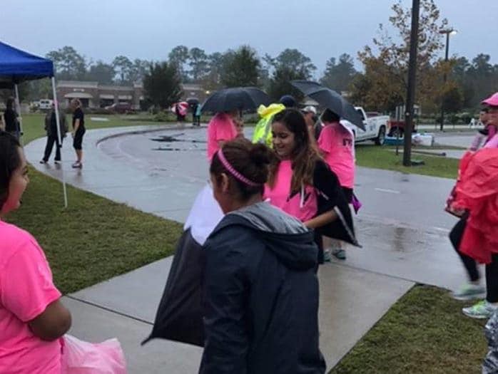 People wearing pink gather outdoors on a rainy day for an event.