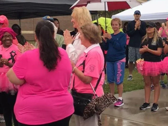 Group of people in pink shirts applauding at an outdoor event.