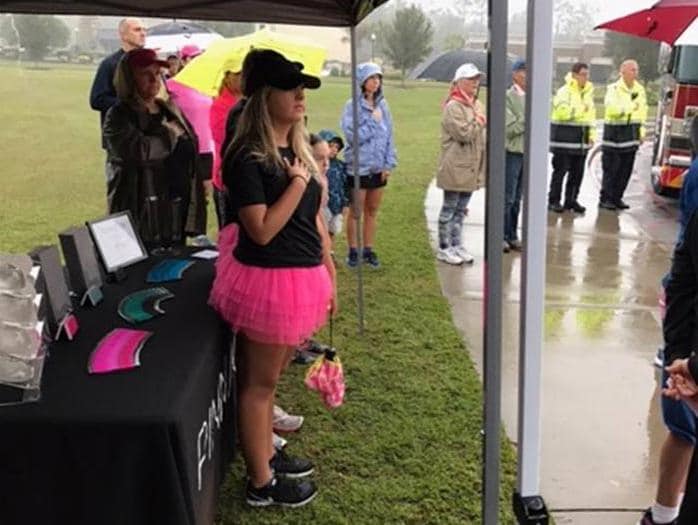 Woman in a black shirt and pink tutu stands with hand on heart