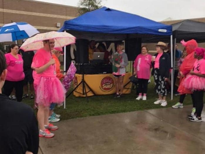 Woman in a pink tutu and umbrella stands near a blue tent.