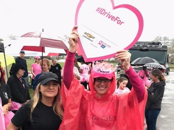 Two women holding an #IDriveFor sign at a breast cancer event