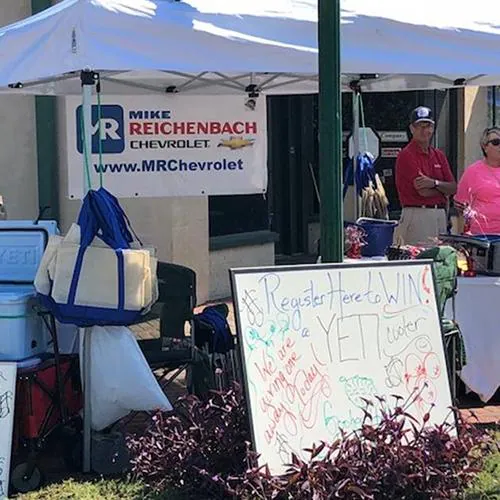 Festival vendor booth with bags, a chalkboard sign, and a banner