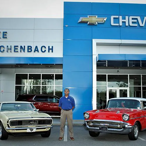 Classic cars and a man stand outside the Chenbach Chevrolet dealership entrance.