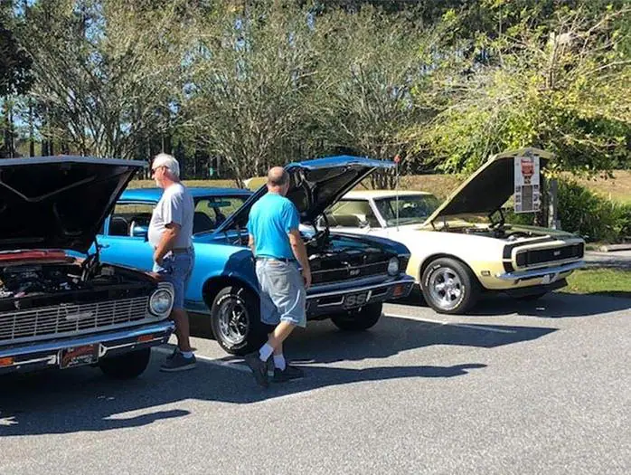 Two men examine a blue classic pickup truck with its hood open