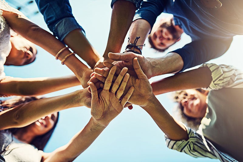 A diverse group of people stacking their hands together in a circle.